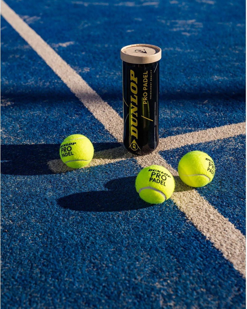 Een koker padelballen en drie ballen op de blauwe baan